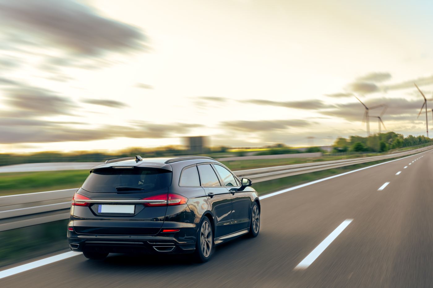 Black estate car driving on an open road at sunset